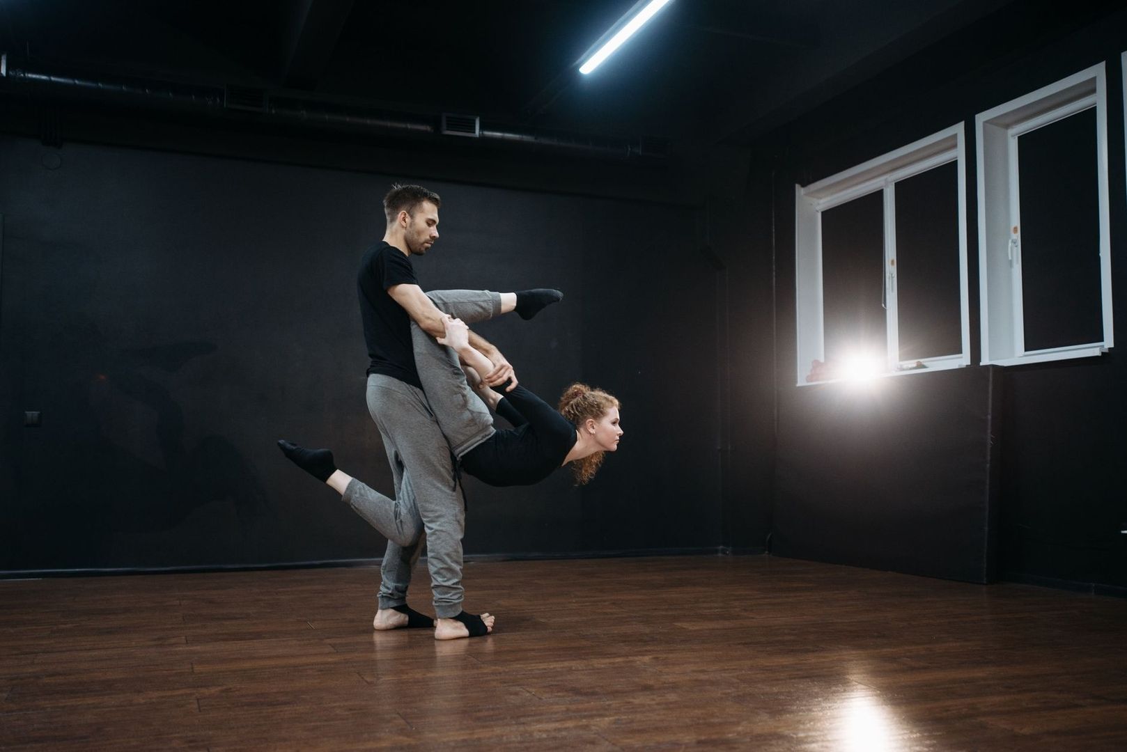 Dance partners practice a lifted move in a dark studio space